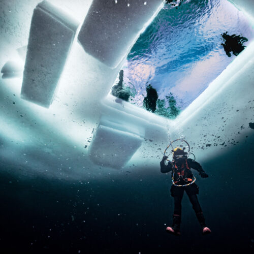 Military divers operating beneath ice, representing extreme underwater operational environments.