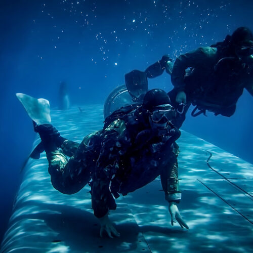 Military divers conducting underwater operations alongside a submarine in the underwater environment